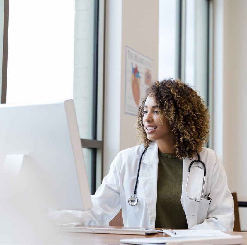 The mid adult female doctor reviews her patient's records on her computer in her office.
